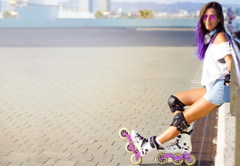 Roller skating young Caucasian girl with violet hair, sunglasses and protection outdoors sitting on...