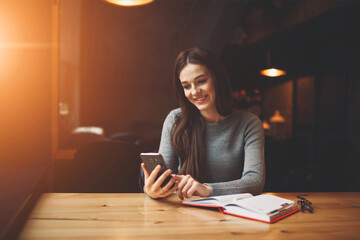 Charming young student feeling happy received good offer on email box while resting in coffee shop, positive administrative manager organizing work while booking using smartphone connected to wifi