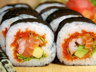 Japanese maki roll with salmon, shrimp, avocado, salad and caviar on a wooden tray close-up