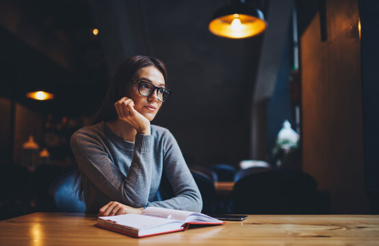  Pensive hipster girl enjoying good day sitting at wooden table in coffee shop