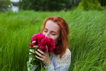 Redhead girl smells peony bouquet in the field