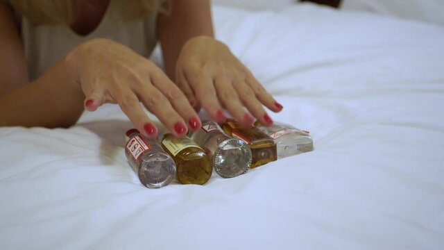 Woman laying in bed of hotel chooses alcohol drinks from mini bar to drink and relax