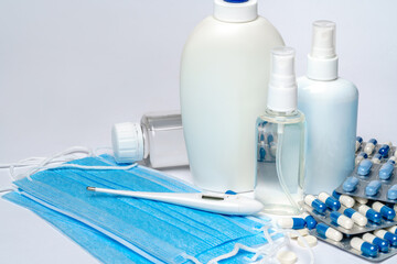 bottle of sanitizer or liquid soap, protective mask, medicine pills blisters and thermometer over light grey background