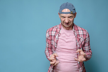 Angry man in a cap and casual clothes looks furiously and makes a gesture with his hands. Copy space.