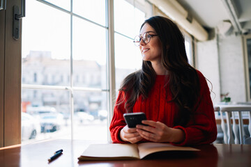 Charming young female author planning working strategy for next book and pondering about title page while sitting in cafe with loft interior,teen pretty hipster girl enjoying leisure time indoors