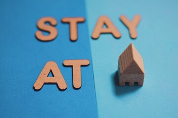 Stay at home message written with 3d wooden alphabet letters and blocks laid on a pair of solid color background. Pandemic situation advice, selective focus.
