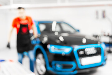 Blurred abstract image of man worker with car in body shop. Blur car auto service. Car bokeh. Blurred background with car in garage. Vehicle maintenance in auto repair service. Blurry service station