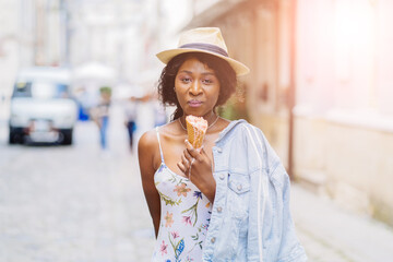 Cheerful black girl in stylish hat with dessert while walking outdoor, selective focus, shallow...