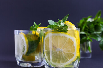 Summer healthy lemonade, cocktails of citrus infused water or mojitos, with lime lemon orange, ice and mint, diet detox beverages, in glasses on gray background.