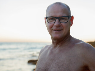 Happy mature handsome tourist man smiling shirtless at the beach