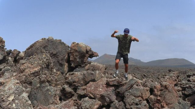 Hombre joven baja de la cima de una roca de lava despu&eacute;s de contemplar el paisaje volc&aacute;nico. Parque Nacional de Timanfaya. Lanzarote. Islas Canarias