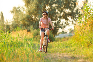 Moments. Joyful young woman riding a bicycle at the riverside and meadow promenade. Inspired by surrounded nature, summertime mood. Warm sunshine colors. Sport, activity, wellness, enjoyment concept.