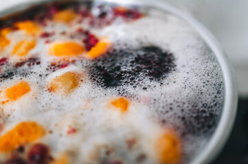 Fresh fruits are boiled in boiling water in a metal pan on a stove with bubbles and foam close-up. Cooking a delicious compote of apricot, apples, cherries, raspberries. Photography, concept.
