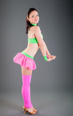 young brunette woman in pink and green dance costume poses at camera smiling
