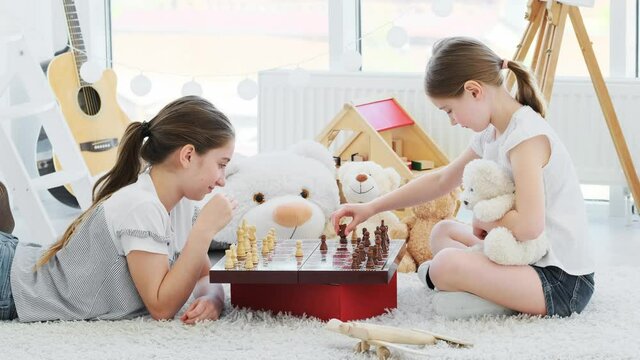 Beautiful sisters playing chess lying on floor in kids room