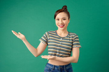 Portrait attractive young Asian woman holding copyspace on the palm isolated on green background.