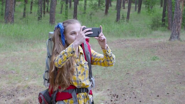Woman with backpack walking in a forest and take a photo with a mobile phone.