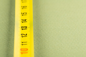 yellow construction measuring tape lies on a table, closeup photo in perspective 13 centimeters; green background