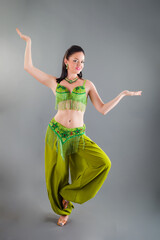 young slim brunette woman in green belly dancer costume poses at camera