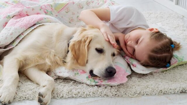 Cute little girl caressing dog head lying under blanket in playroom