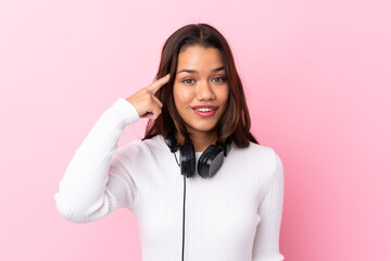 Fototapeta premium Young woman with earphones over isolated pink wall intending to realizes the solution