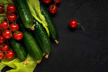 Red wet cherry tomatoes and green cucumbers on green gauze and dark textured background. Top view. Space for text.