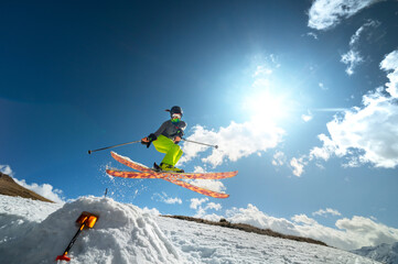 Girl skier in flight after jumping from a kicker in the spring against the backdrop of mountains and blue sky. Close-up wide angle. The concept of closing the ski season and skiing in spring
