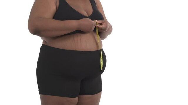 close-up of unrecognizable african obese woman's body in underwear measuring her breast size isolated on white background