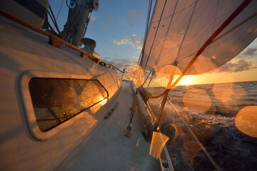 White sailboat in an open sea at sunset. Single handed sailing a 34 ft yacht. Close-up view of the...