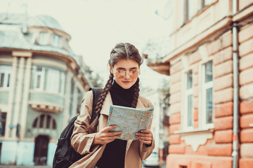 Traveler girl with cute braids looking at a map, searching right direction over blurred city background.