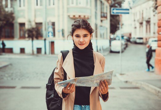 Young inspired female enjoying her trip, waking down the street with city-map in hands.