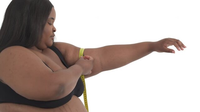 Close-up of african american woman with overweight in underwear measuring her upper arm isolated on white background