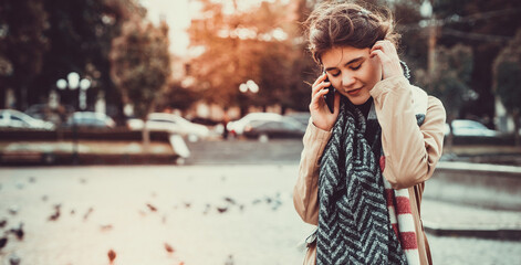 Fototapeta premium Pretty teen girl strolling on a square full of doves, talking on phone and enjoying the last warm days in a year.