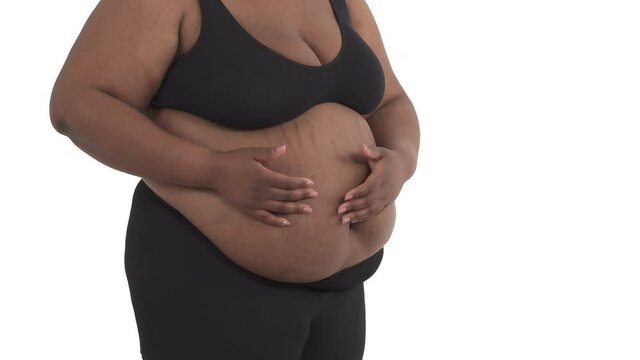 Close-up of unrecognizable black obese woman's body in underwear shaking her fat from her belly and showing thumb down isolated on white background