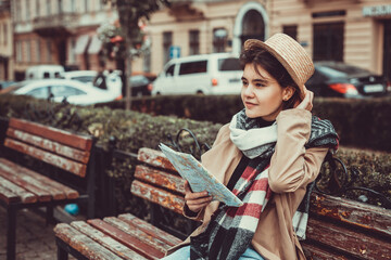 Lady excited about visiting new places, holding a map in hand, weared in trendy coat and hat over...