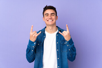 Teenager caucasian  handsome man isolated on purple background making rock gesture