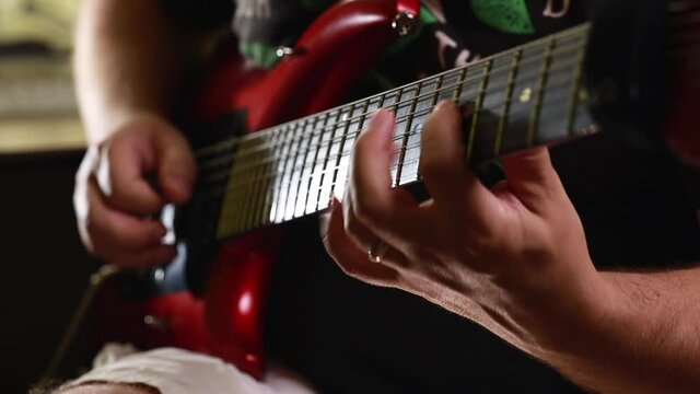 Close-up of a man playing a red electrical guitar in a music studio