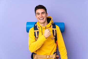 Teenager caucasian mountaineer man with a big backpack isolated on purple background celebrating a victory