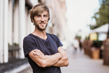 Handsome smiling young man portrait. Cheerful men with crossed arms looking at camera in city....