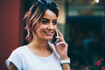 Stylish cheerful hipster girl with pink hair and sunglasses on head talking on digital smartphone...