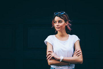 Thoughtful young woman with stylish pink hair and sunglasses on head dressed in white t-shirt with...