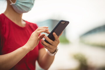 Asian woman wearing face mask using smartphone in modern city