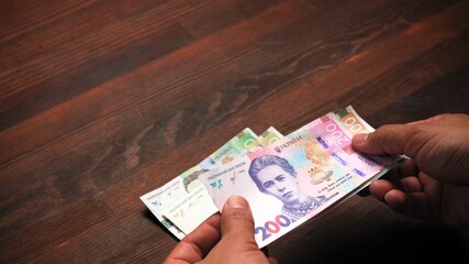 Male hands counts paper money holding pack of new Ukrainian banknotes, hryvnias on wooden table. Exchange, concept. Close up shot.