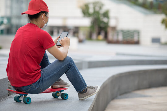 Asian woman sit on skateboard using smartphone in modern city