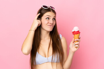 Young caucasian woman in swimsuit holding a cornet ice cream isolated on pink background having...