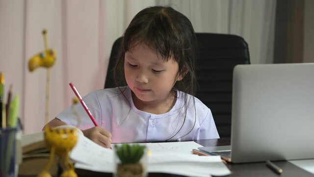 Asian little girl in preschool uniform doing school homework drawing and painting at home her was intending to do home work to send the teacher the next day