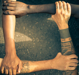 Multiracial people with black, latin, caucasian and asian hands holding each other arms in...