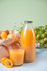 Bottle and glass of fresh apricot juice and plate of apricot on the background