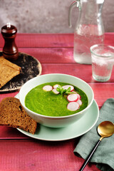 A plate with vegan green spinach cream soup on red rustic wooden table