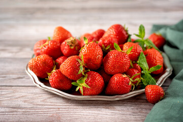 Close up of a plate with red and juicy strawberry on gray wooden background